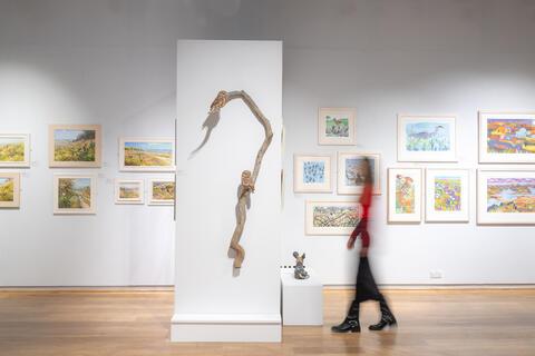 Person walking across gallery next to sculptures and painting