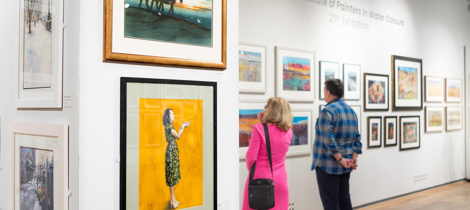 Two people looking at paintings in an exhibition