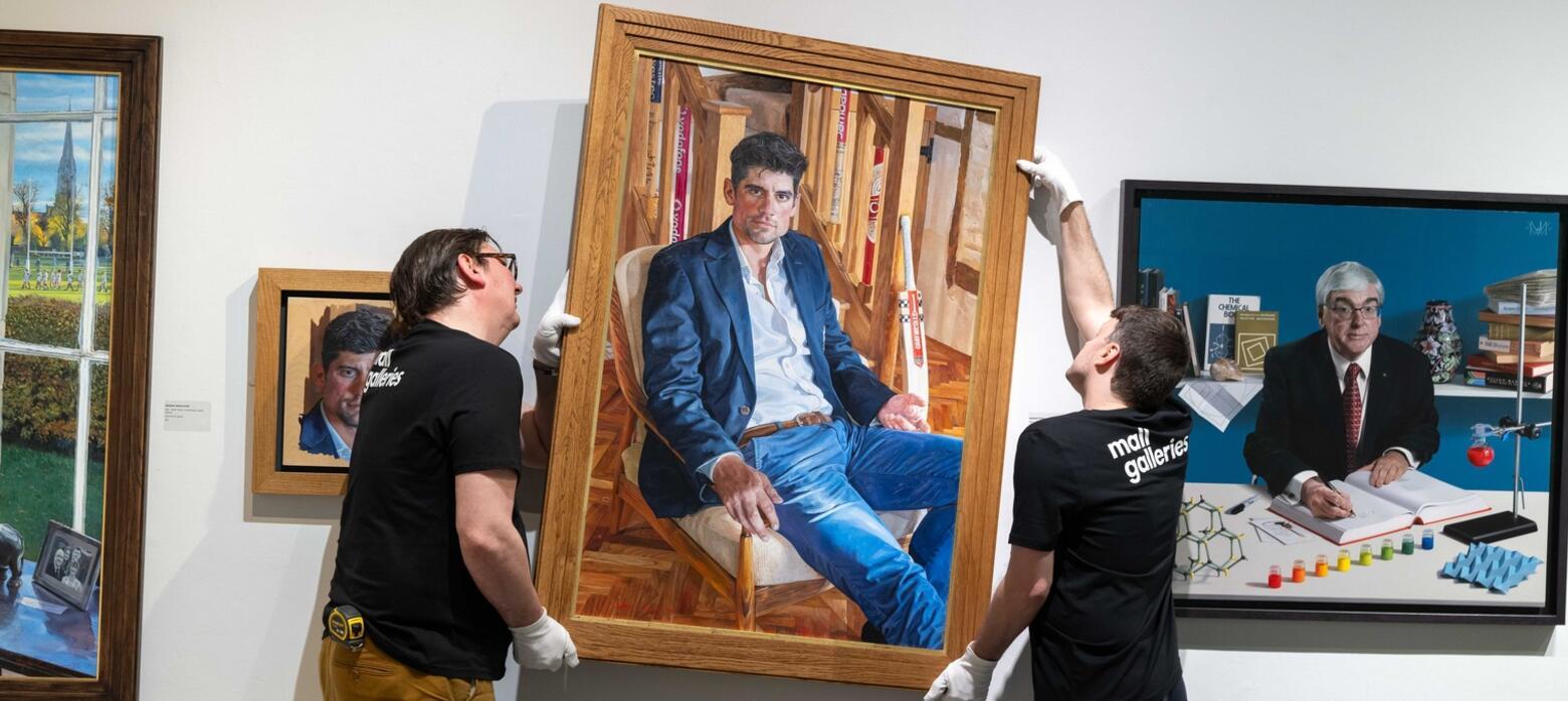 Two men hanging a portrait on the wall