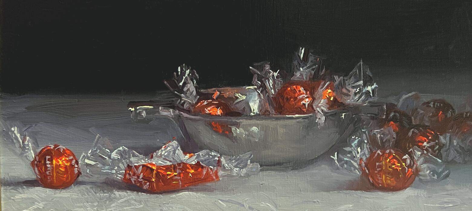 a silver bowl with round chocolates in red wrappers inside and surrounding it