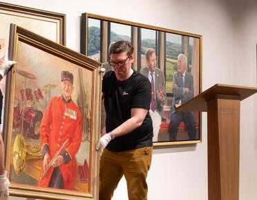 Photo of Robert Luck moving a portrait during the RP annual exhibition 2024