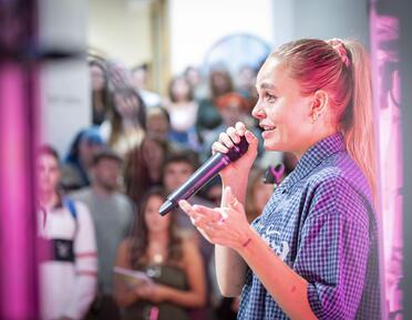 Person with blonde hair in a pony tail speaking into microphone