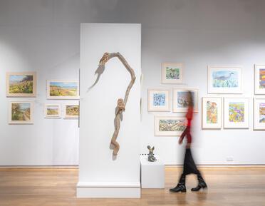 Person walking across gallery next to sculptures and painting