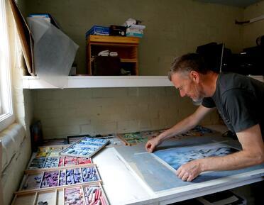 Artist Dave Roberts PS in his studio, taping a pastel drawing to a board.. 