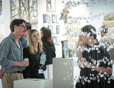 two people looking at a hanging sculpture of small paper houses